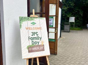 A wooden easel holding a welcome sign that reads "Welcome to JPC Family Day at Dublin Zoo" with cartoon animal illustrations, standing outside an open doorway.