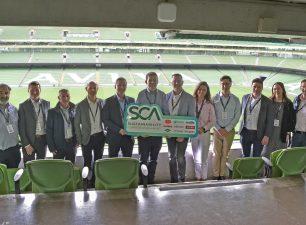 John Paul Construction team members and founding industry partners holding a large green launch sign for the Sustainability Common Assessment (SCA) inside a stadium box overlooking the pitch at the Aviva Stadium, Dublin.